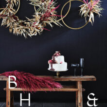 Food photography of white and pink wedding cake topped with pink raspberries and flowers in front of black background