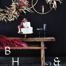 Food photography of white and pink wedding cake topped with pink raspberries and flowers in front of black background