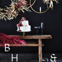 Food photography of white and pink wedding cake topped with pink raspberries and flowers in front of black background