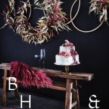 Food photography of white and pink wedding cake topped with pink raspberries and flowers in front of black background