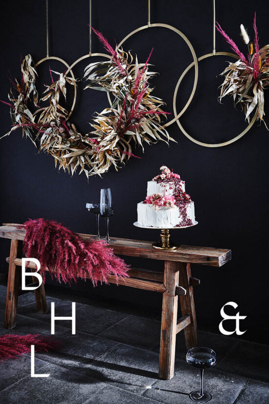 Food photography of white and pink wedding cake topped with pink raspberries and flowers in front of black background