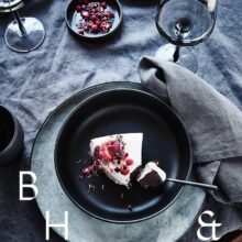 Food photography of white and pink cake with chocolate and dried berries in a black table setting with dark linen and black tableware decorated with dry bamboo in scandinavian industrial loft