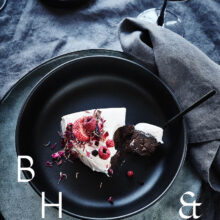 Food photography of white and pink cake with chocolate and dried berries in a black table setting with dark linen and black tableware decorated with dry bamboo in scandinavian industrial loft
