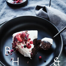 Food photography of white and pink cake with chocolate and dried berries in a black table setting with dark linen and black tableware decorated with dry bamboo in scandinavian industrial loft
