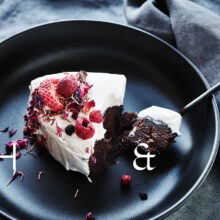 Food photography of white and pink cake with chocolate and dried berries in a black table setting with dark linen and black tableware decorated with dry bamboo in scandinavian industrial loft
