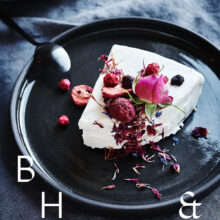 Food photography of white and pink cake with chocolate and dried berries in a black table setting with dark linen and black tableware decorated with dry bamboo in scandinavian industrial loft