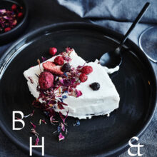 Food photography of white and pink cake with chocolate and dried berries in a black table setting with dark linen and black tableware decorated with dry bamboo in scandinavian industrial loft