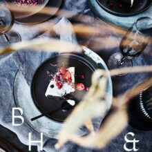 Food photography of white and pink cake with chocolate and dried berries in a black table setting with dark linen and black tableware decorated with dry bamboo in scandinavian industrial loft
