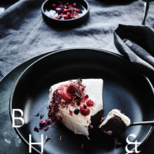Food photography of white and pink cake with chocolate and dried berries in a black table setting with dark linen and black tableware decorated with dry bamboo in scandinavian industrial loft