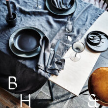 Interior photography of black table setting with dark linen and black tableware decorated with dry bamboo in scandinavian industrial loft