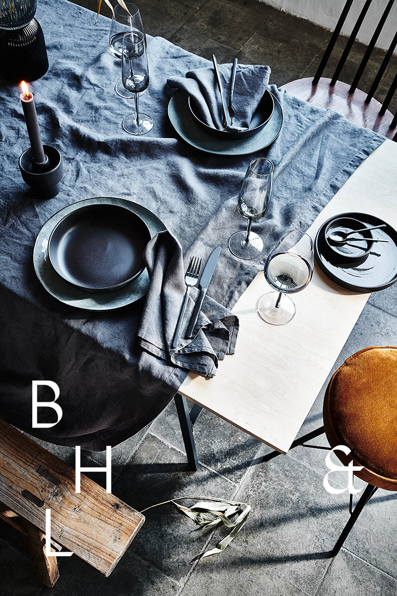 Interior photography of black table setting with dark linen and black tableware decorated with dry bamboo in scandinavian industrial loft