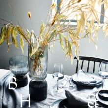 Interior photography of black table setting with dark linen and black tableware decorated with dry bamboo in scandinavian industrial loft