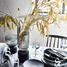 Interior photography of black table setting with dark linen and black tableware decorated with dry bamboo in scandinavian industrial loft