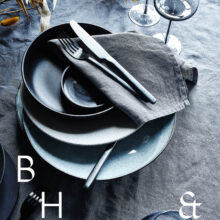 Interior photography of black table setting with dark linen and black tableware decorated with dry bamboo in scandinavian industrial loft