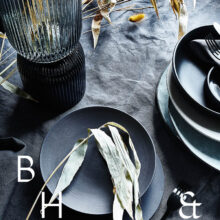 Interior photography of black table setting with dark linen and black tableware decorated with dry bamboo in scandinavian industrial loft