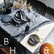 Interior photography of black table setting with dark linen and black tableware decorated with dry bamboo in scandinavian industrial loft