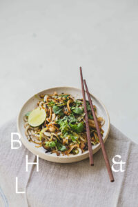 Thai dish with asian noodles, cilantro, mushrooms and black sesame on a white plate and linen