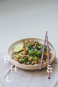 Thai dish with asian noodles, cilantro, mushrooms and black sesame on a white plate and linen