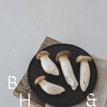 Food photography of french horn mushroom on a black plate with natural tones towels on a bench