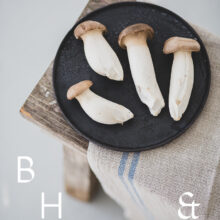 Food photography of french horn mushroom on a black plate with natural tones towels on a bench