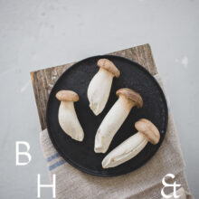 Food photography of french horn mushroom on a black plate with natural tones towels on a bench