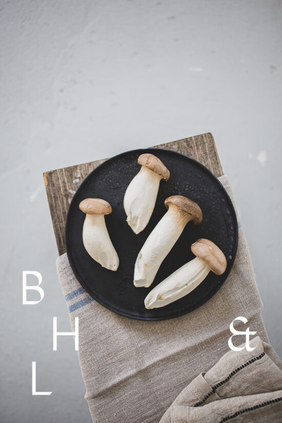 Food photography of french horn mushroom on a black plate with natural tones towels on a bench