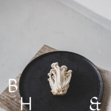 Food photography of enoki mushrooms on a black plate on a bench in perspective