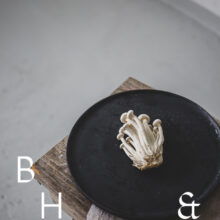 Food photography of enoki mushrooms on a black plate on a bench in perspective