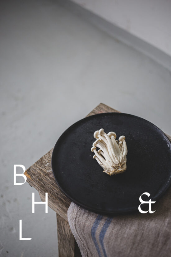 Food photography of enoki mushrooms on a black plate on a bench in perspective