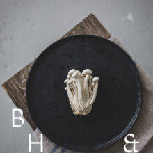Food photography of enoki mushrooms on a black plate on a bench as a top shot