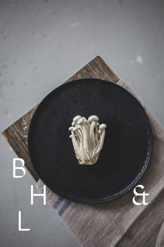 Food photography of enoki mushrooms on a black plate on a bench as a top shot