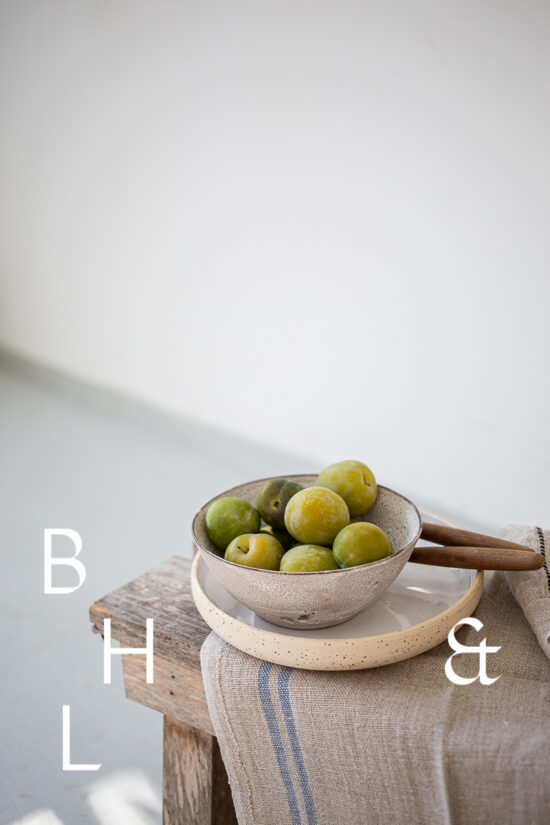 Foodphotography of reneclode in bowl on wooden bench in front of while wall