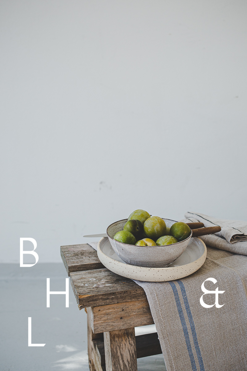 Foodphotography of reneclode in bowl on wooden bench in front of while wall