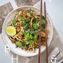 Food photography of Thai noodles with lime and Thai basil on a white ceramic plate with chopsticks on a linen towels as a table top shoot