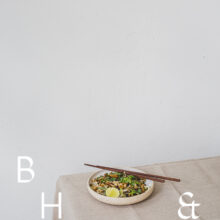 Food photography of Thai noodles with lime and Thai basil on a white ceramic plate with chopsticks on a linen tablecloth with negative space