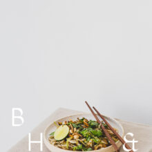Food photography of Thai noodles with lime and Thai basil on a white ceramic plate with chopsticks on a linen tablecloth with negative space