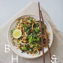 Food photography of Thai noodles with lime and Thai basil on a white ceramic plate with chopsticks on a linen tablecloth as a table top shoot