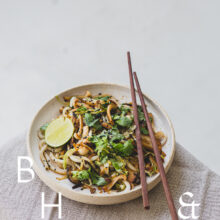 Food photography of Thai noodles with lime and Thai basil on a white ceramic plate with chopsticks on a linen tablecloth shoot from above