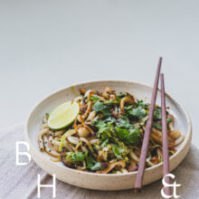 Food photography of Thai noodles with lime and Thai basil on a white ceramic plate with chopsticks on a linen tablecloth shoot in perspective
