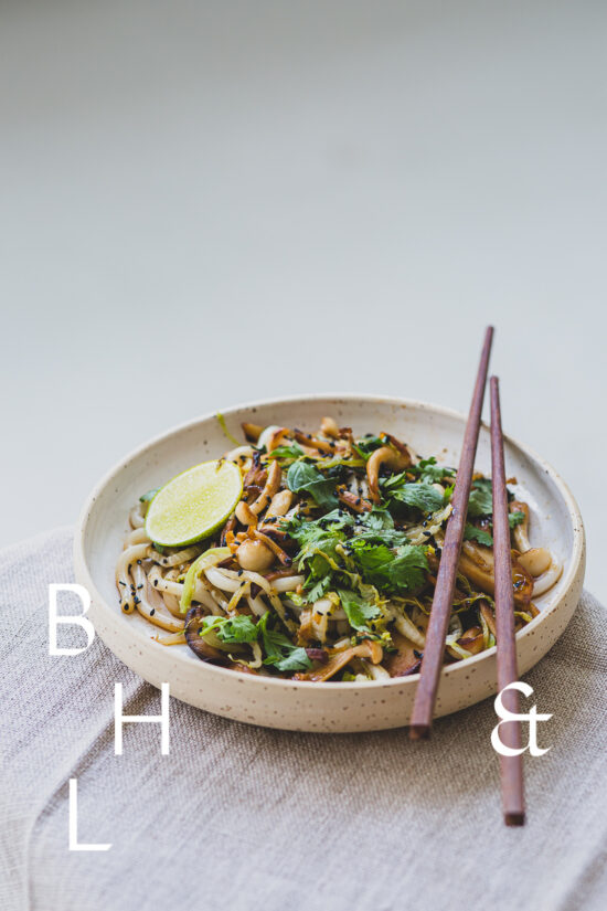 Food photography of Thai noodles with lime and Thai basil on a white ceramic plate with chopsticks on a linen tablecloth shoot in perspective