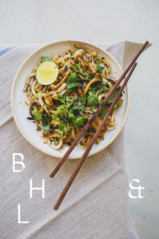 Food photography of Thai noodles with lime and Thai basil on a white ceramic plate with chopsticks on a linen tablecloth as a table top shoot