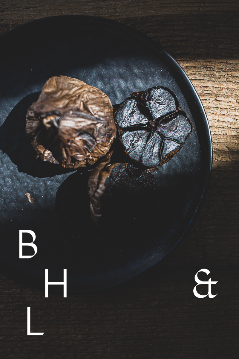 Food photography of black garlic on a black plate cut open