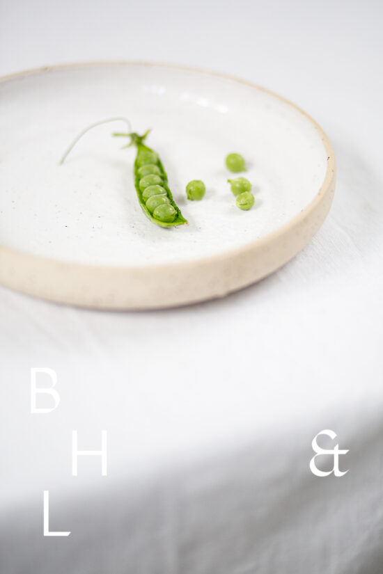 Food photography of a pea pod on a white plate on a white table clove in perspective