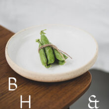 Food photography of a pea pod on a white plate on a wooden chair from the side
