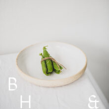 Food photography of a pea pod tied together on a white plate on white table clove