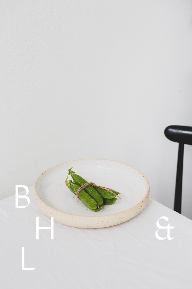 Food photography of a pea pod on a white plate on white table clove with a black chair