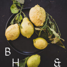 Food photography of lemons and lemon leaves on a black plate set on a black table