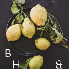 Food photography of lemons and lemon leaves on a black plate set on a black table