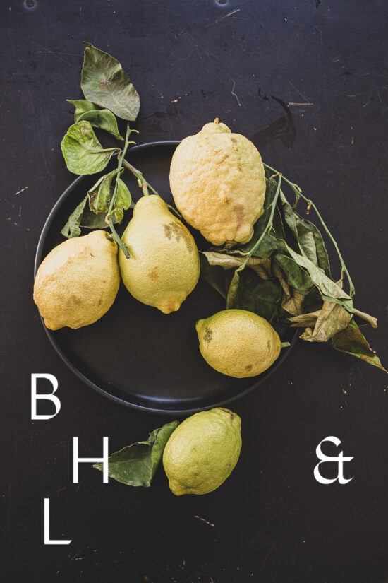 Food photography of lemons and lemon leaves on a black plate set on a black table