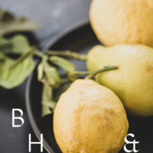 Food photography of lemons and lemon leaves on a black plate set on a black table